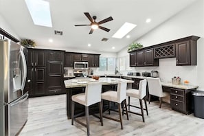 A modern kitchen with dark cabinets, stainless steel appliances, and a central island with bar stools. - Kierland Palms-Pool & Spa-Near Kierland Commons (Scottsdale)