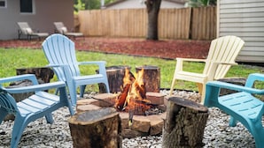 Een achtertuin met een vuurkorf, omringd door Adirondack-stoelen.