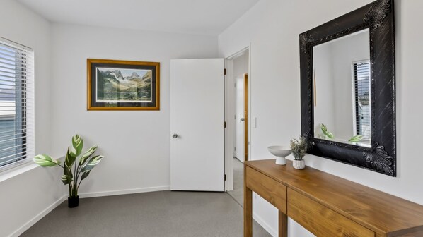 A hallway with a wooden console table, a framed landscape painting, a potted plant, and a large mirror with an ornate frame.