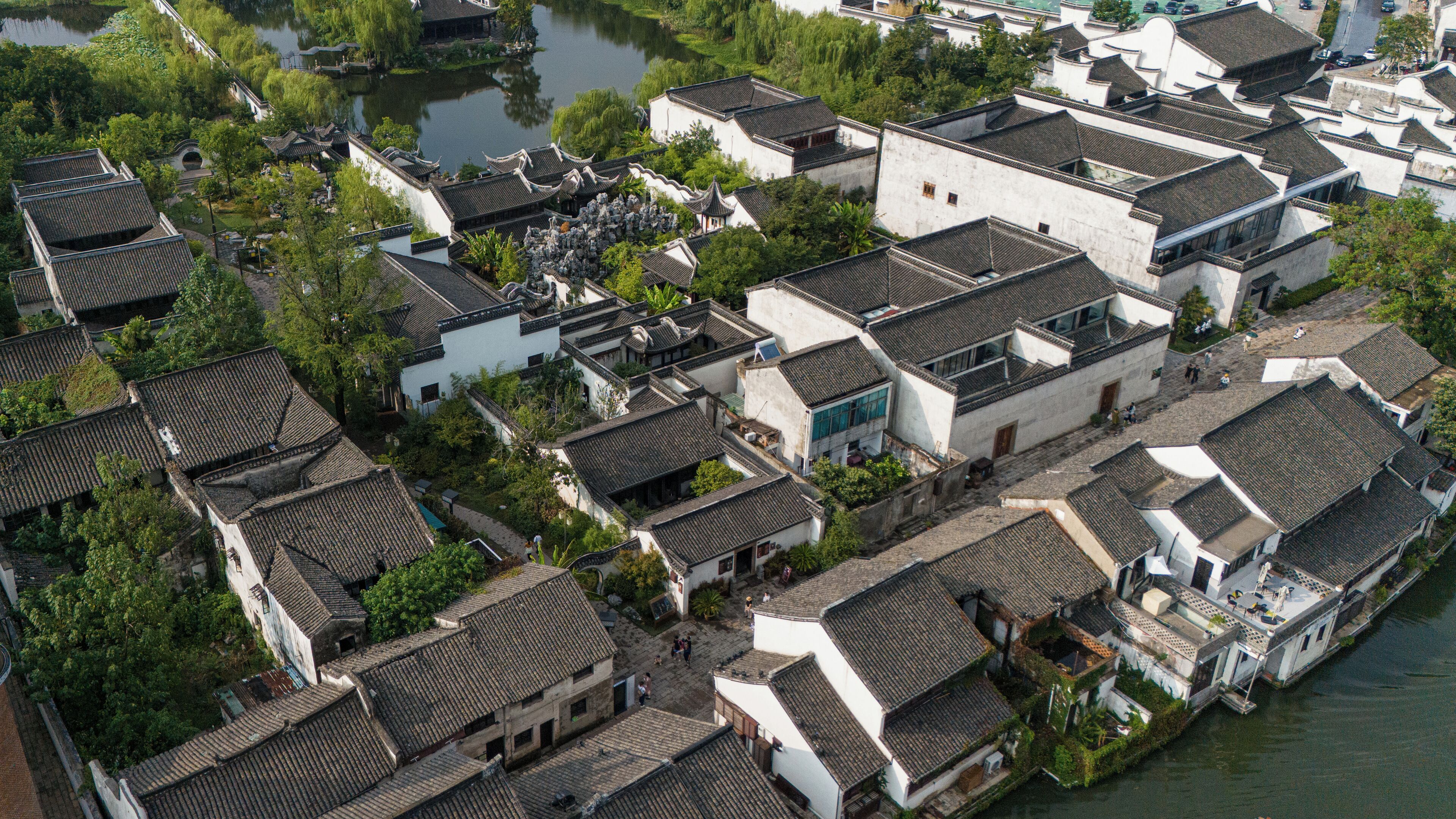 An aerial view of a traditional Chinese village with narrow streets, white buildings, and a river.