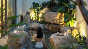 A woman sitting by a small water feature surrounded by rocks and plants, with candles and a bottle of wine on the rocks. - Jiangnanfu Bed and Breakfast (Huzhou)