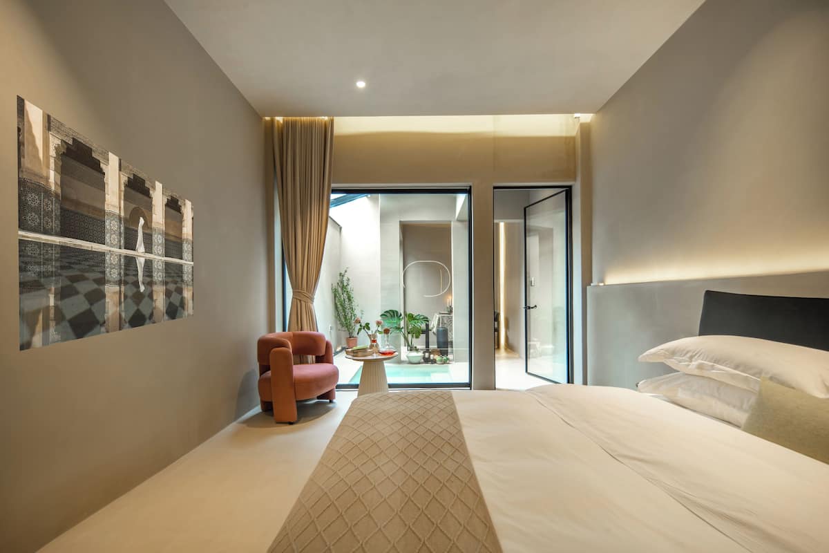 A modern hotel room with a large bed, a small seating area, and a view of the outdoor space.
