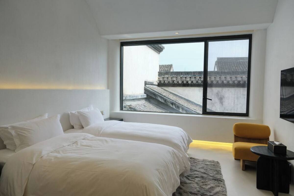 A modern bedroom with a large window, a bed, a sofa, and a small table.