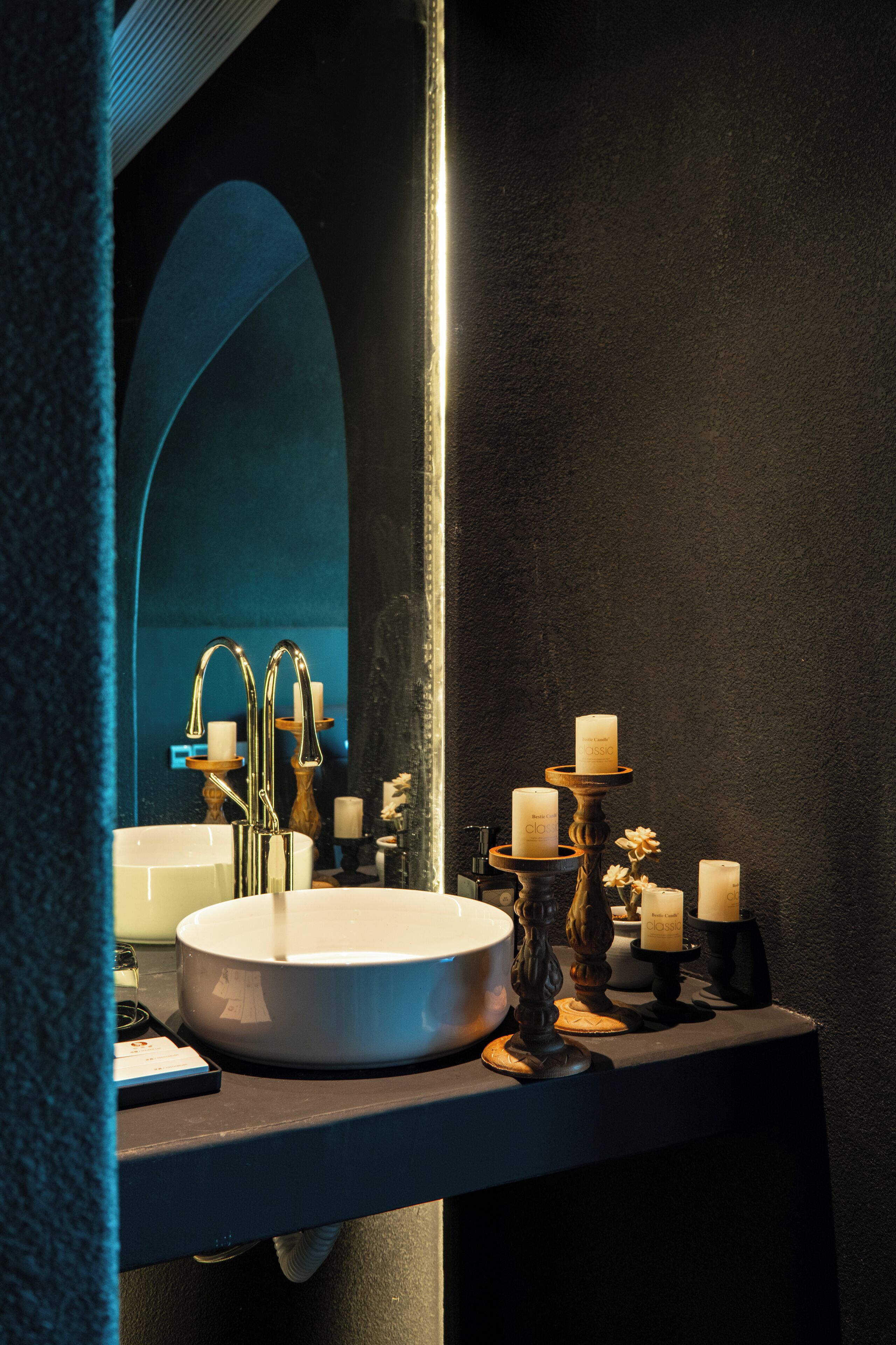 Un baño con un lavabo redondo, un espejo y velas sobre una encimera oscura.