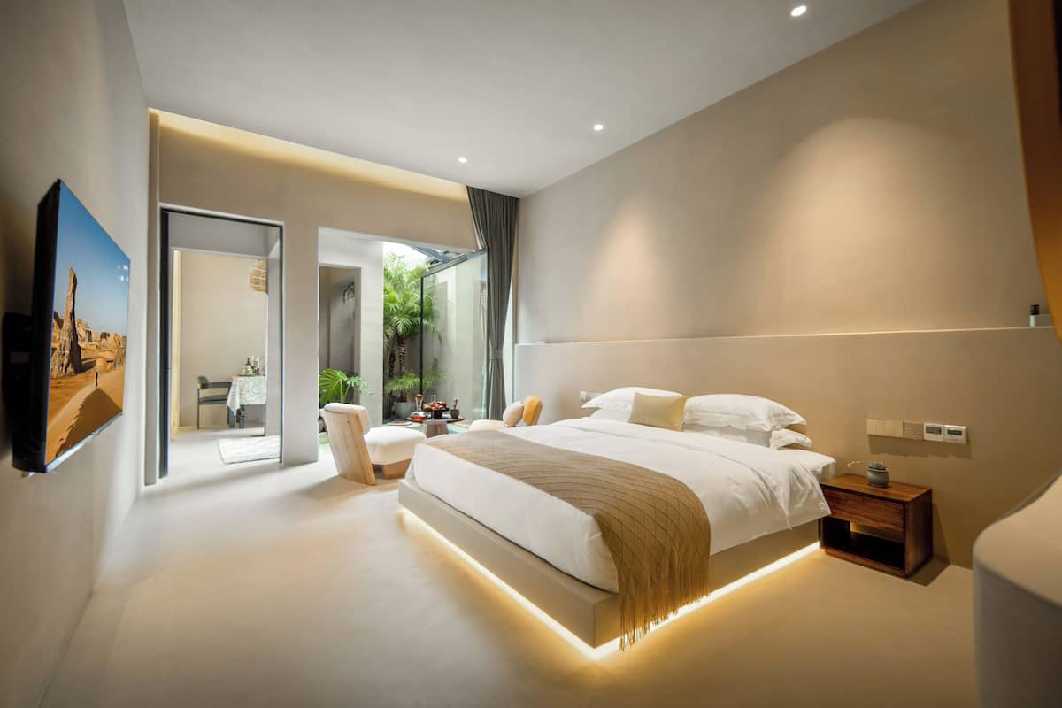 A modern bedroom with a large bed, bedside tables, a TV, and a glass door leading to a bathroom.