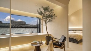 A modern bedroom with a large window, a potted tree, a reading area with books, and a bed with a white duvet. - Jiangnanfu Bed and Breakfast (Huzhou)