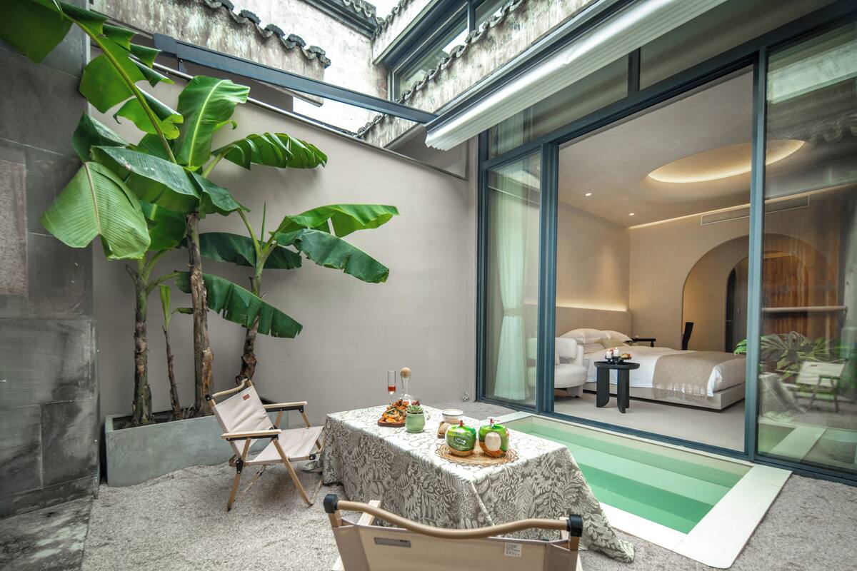 A modern hotel room with a large window, a bed, a bedside table, and a view of the outside.