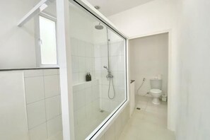 A modern bathroom with a glass-enclosed shower, white tiles, a toilet, and a small shelf with toiletries. - Spacious 8Br Private Pool Villa in Chalong (Phuket)