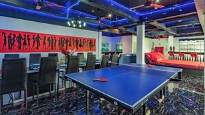 Une pièce avec une table de ping-pong, des chaises, un canapé rouge et un mur orné de silhouettes.