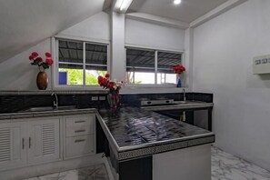 A kitchen with a black and white tiled backsplash, a window with a view, and a vase with red flowers. - Spacious 8Br Private Pool Villa in Chalong (Phuket)