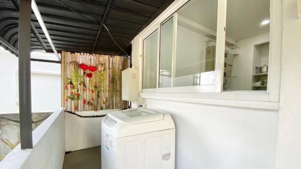 Een wasruimte met een wasmachine, een raam met uitzicht en een gordijn met een bloemenprint.