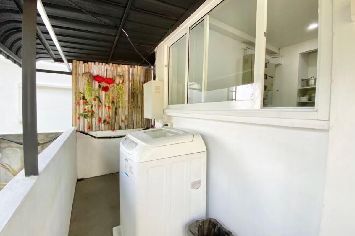 A laundry area with a washing machine, a window with a view, and a curtain with a floral pattern.
