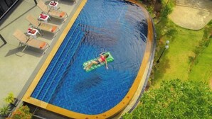 Une piscine avec une personne sur un flotteur, entourée de chaises longues et de verdure.