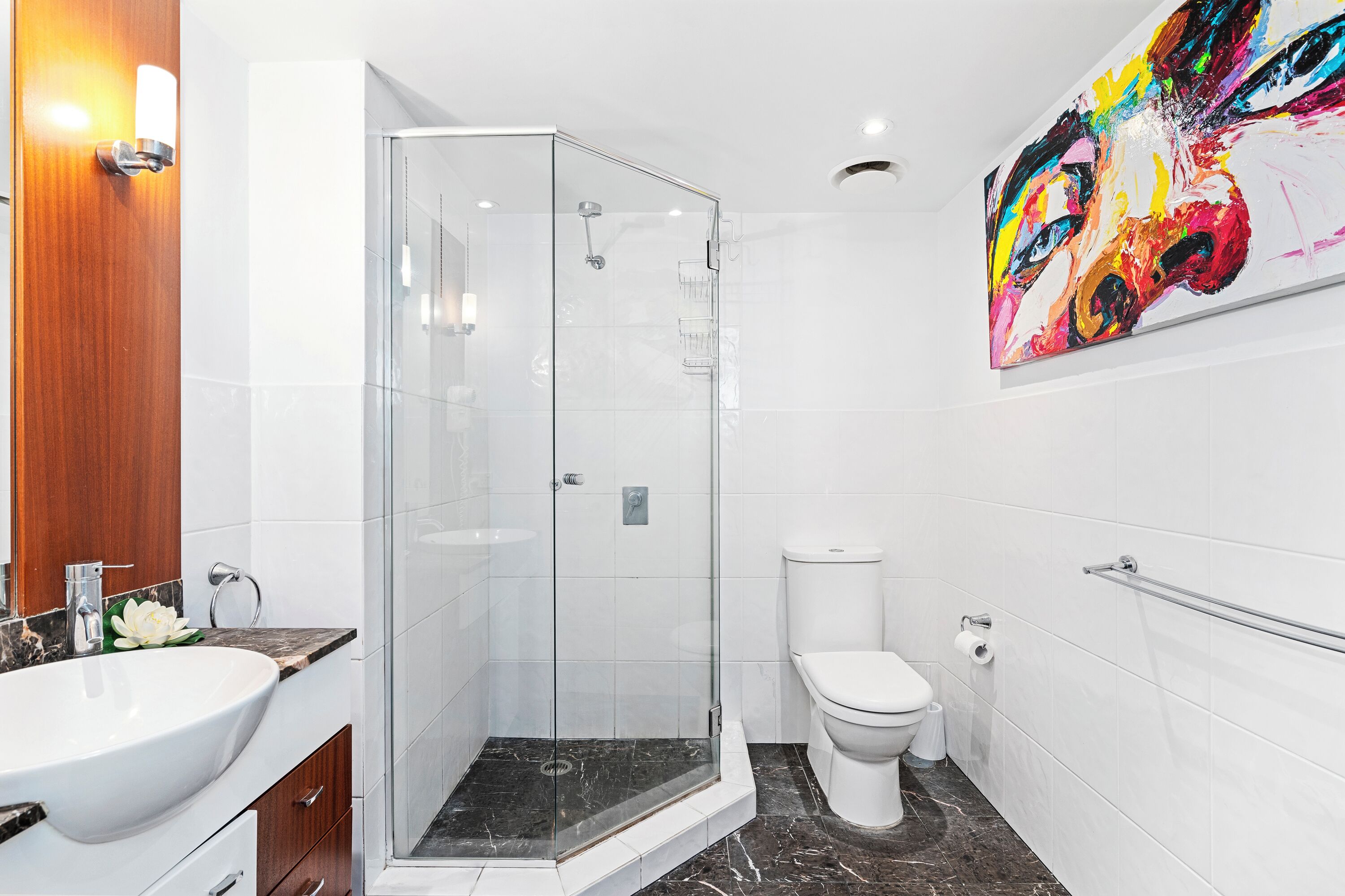 A modern bathroom with a glass-enclosed shower, a white sink, and a toilet.