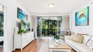 A modern living room with a glass coffee table, white sofa, and artwork on the walls. - Chevron Renaissance Garden View (Surfers Paradise)