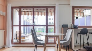 Un appartement moderne doté d’un coin repas, d’une cuisine avec un bar et de grandes fenêtres offrant une vue sur la ville.