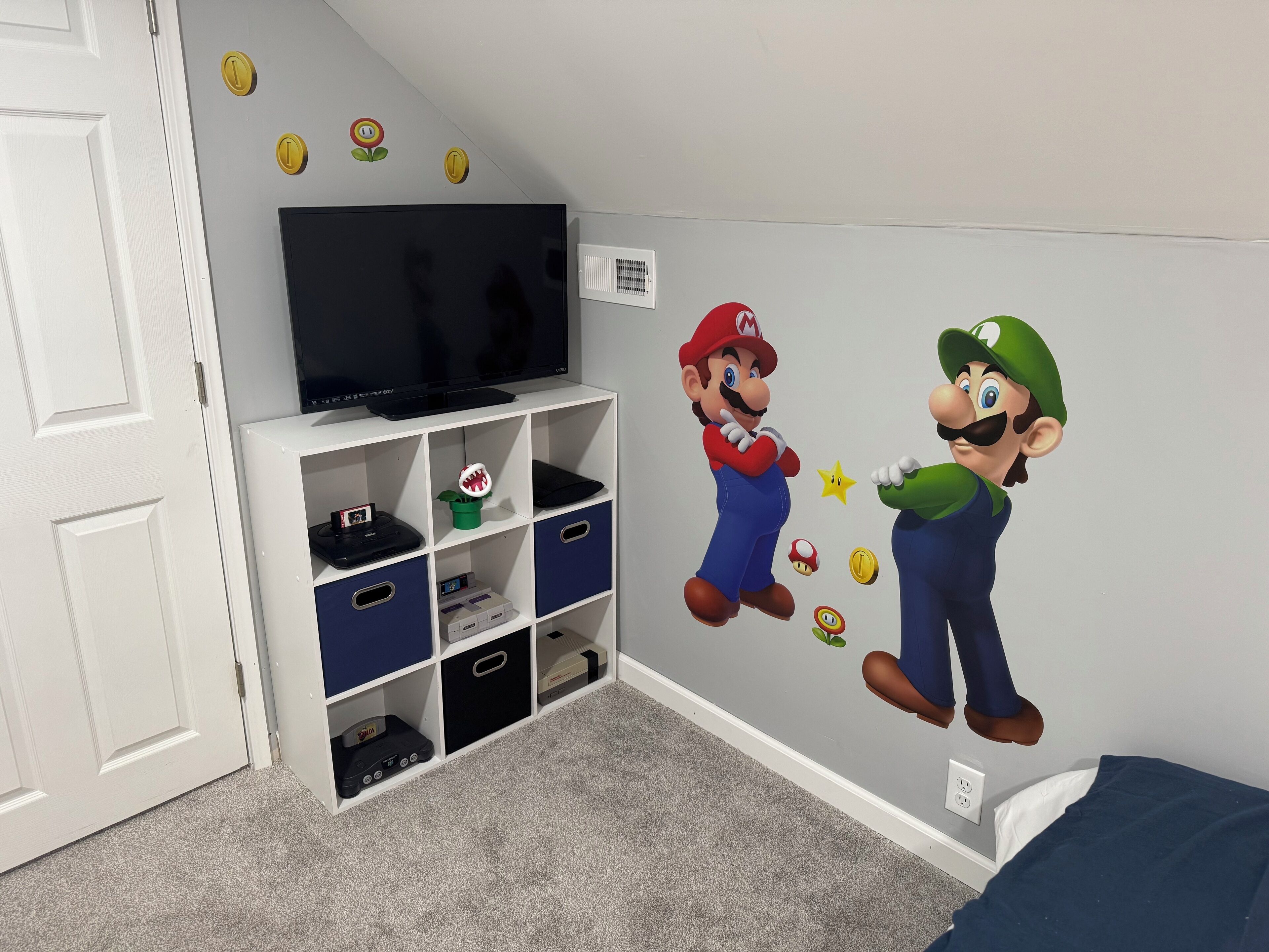 A bedroom with a white door, a TV on a white shelf, and Mario and Luigi wall decals.