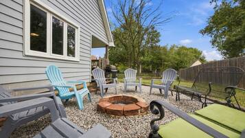 A patio with Adirondack chairs, a fire pit, and a grill area.