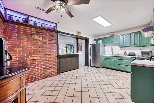 Una cocina con gabinetes verdes, pared de ladrillo y ventilador de techo.
