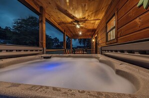Un jacuzzi en una cabaña de madera con ventilador de techo y vistas al exterior.