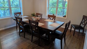 A dining room with a wooden table, six chairs, two pendant lights, and windows with a view of trees. - 4-bedroom house in Ithaca, 5 min from Cornell Graduation (Ithaca)