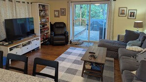 A living room with a television, bookshelves, a black leather chair, a sofa, and a dining area with chairs. - 4-bedroom house in Ithaca, 5 min from Cornell Graduation (Ithaca)