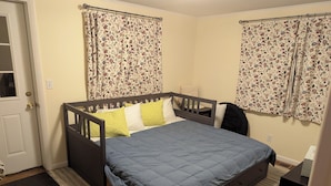 A bedroom with a bed, a wooden headboard, a nightstand, a chair, and floral curtains. - 4-bedroom house in Ithaca, 5 min from Cornell Graduation (Ithaca)