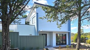 Una casa moderna de dos pisos con fachada blanca, ventanas amplias y una cerca verde.