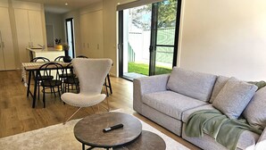 Una sala de estar moderna con un sofá gris, una mesa de centro redonda y una zona de comedor con una mesa y sillas.