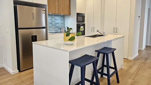Una cocina moderna con muebles blancos, un refrigerador de acero inoxidable, un microondas y un lavamanos.