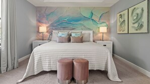Een slaapkamer met een groot bed, twee nachtkastjes, een wanddecoratie en twee poefs.