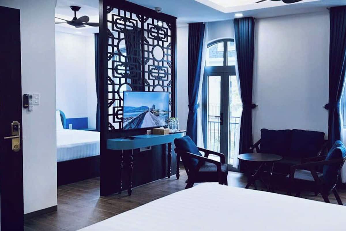 Ein Hotelzimmer mit Bett, Schreibtisch mit Computer, Stuhl, kleinem Tisch und Blick auf die Stadt durch ein Fenster.