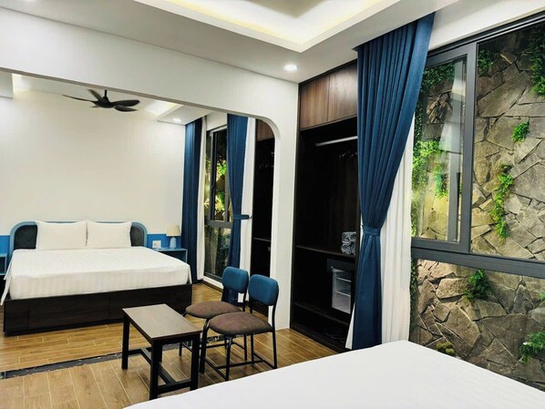 A modern bedroom with a bed, a desk, and chairs. There is a window with curtains and a view of greenery outside.