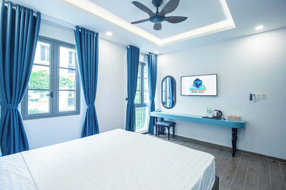 Ein Hotelzimmer mit einem Bett, einem Schreibtisch mit Spiegel, einem Deckenventilator und einem Fenster mit Vorhängen.