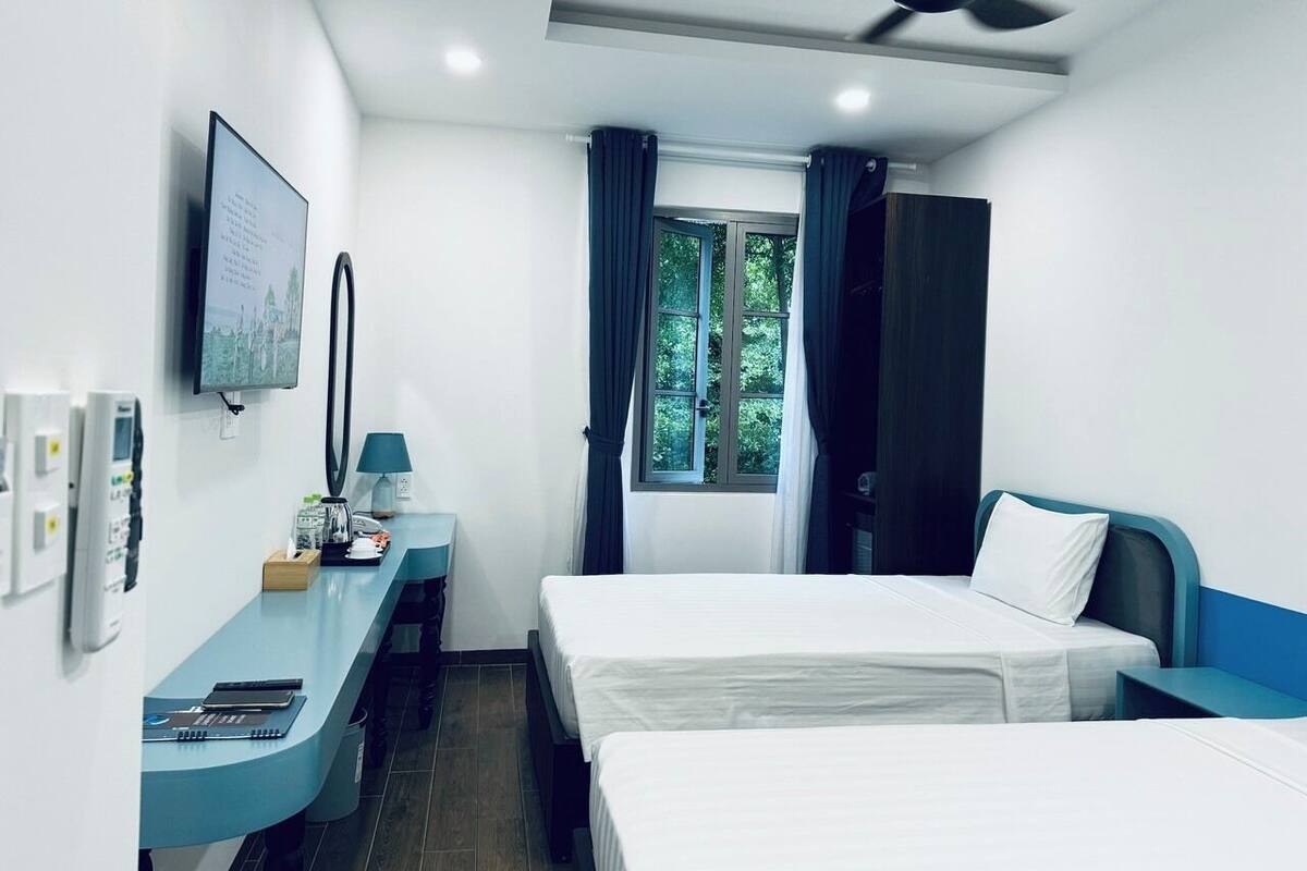 Ein Hotelzimmer mit einem Bett, einem Schreibtisch mit Lampe, einem Fernseher und einem Fenster mit Vorhängen.