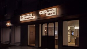 Das äußere Erscheinungsbild des Hotels The Cozies auf der Erde, mit einer modernen Fassade, beleuchteter Beschilderung und einem sichtbaren Eingang.