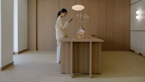 Eine Person steht an einem Holztisch in einem Raum mit einer Holzwand und einer Deckenleuchte.