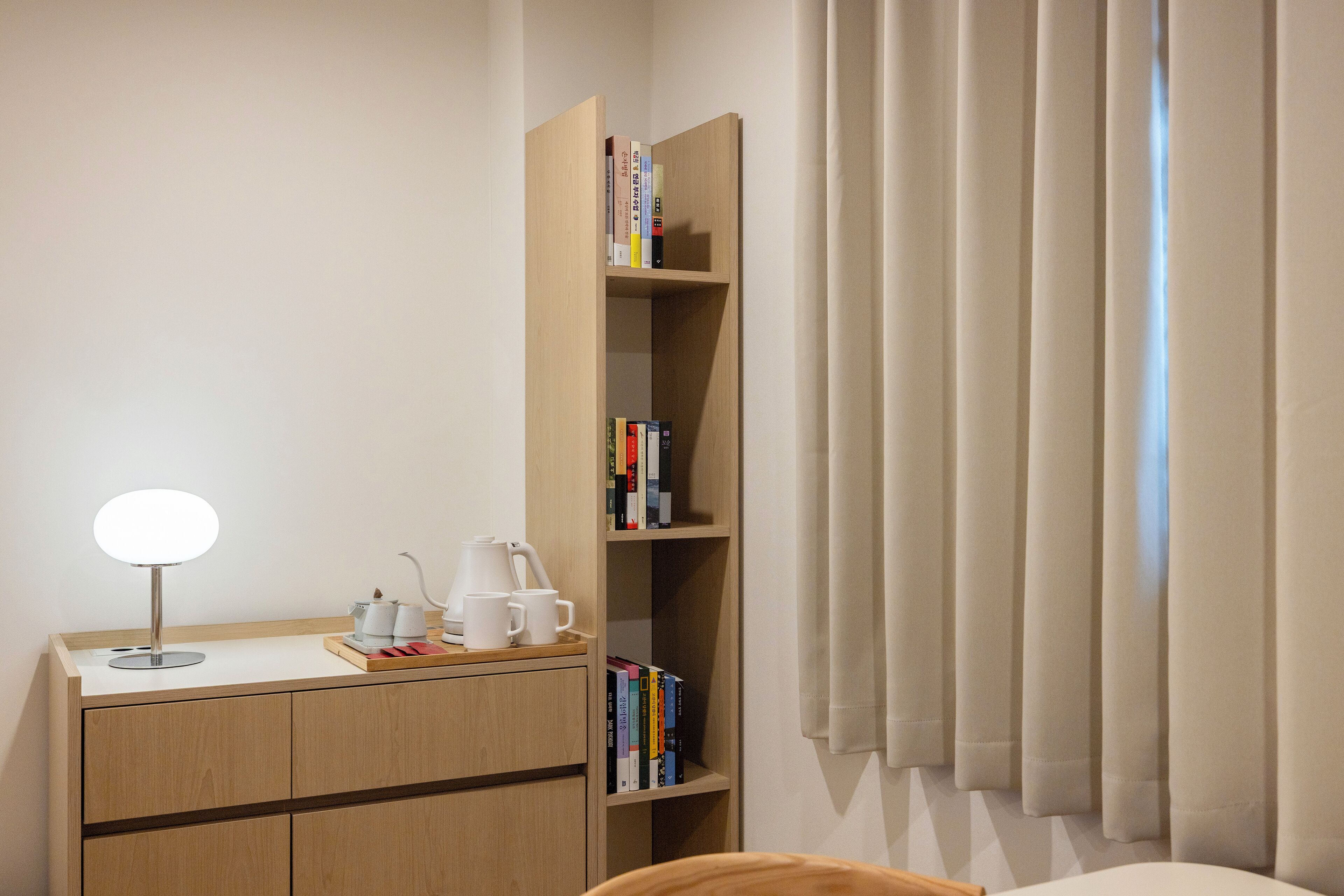 Habitación de hotel con un escritorio de madera, una lámpara, una estantería y una ventana con cortinas.