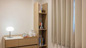 Habitación de hotel con un escritorio de madera, una lámpara, una estantería y una ventana con cortinas.