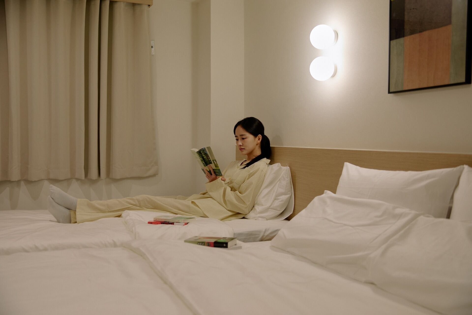 Eine Person liegt in einem Hotelzimmer in einem Bett und liest ein Buch.