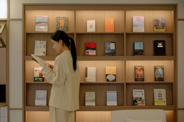 A person reading a book in a library with shelves of books. - Aank Hotel Cheongnyangni (Seoul)