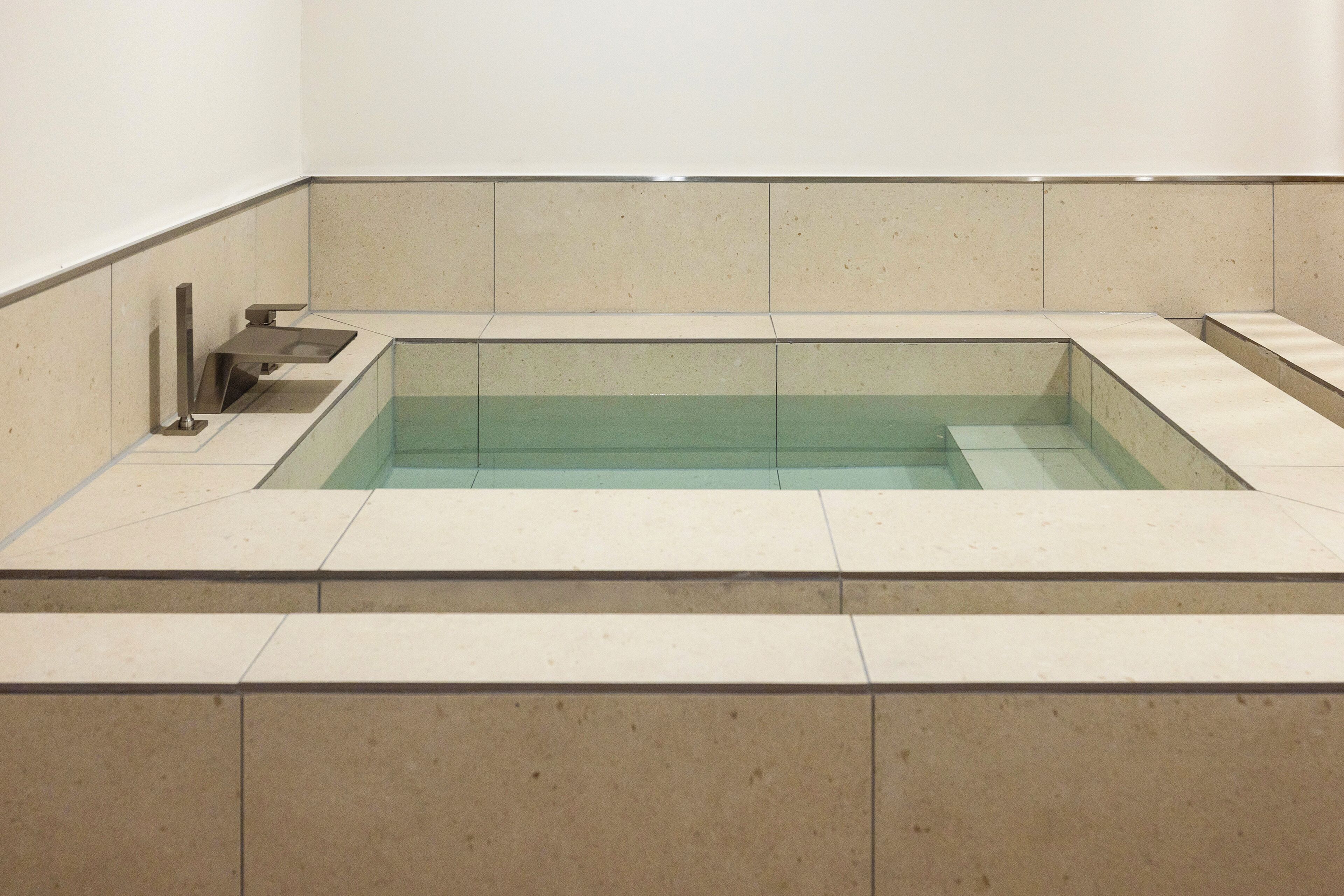 Una piscina rectangular amb aigua cristal·lina, envoltada de rajoles beix.