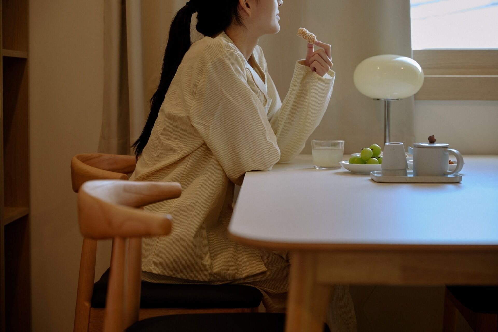 Una persona sentada a una mesa con una lámpara, un plato de uvas verdes y un vaso de leche.