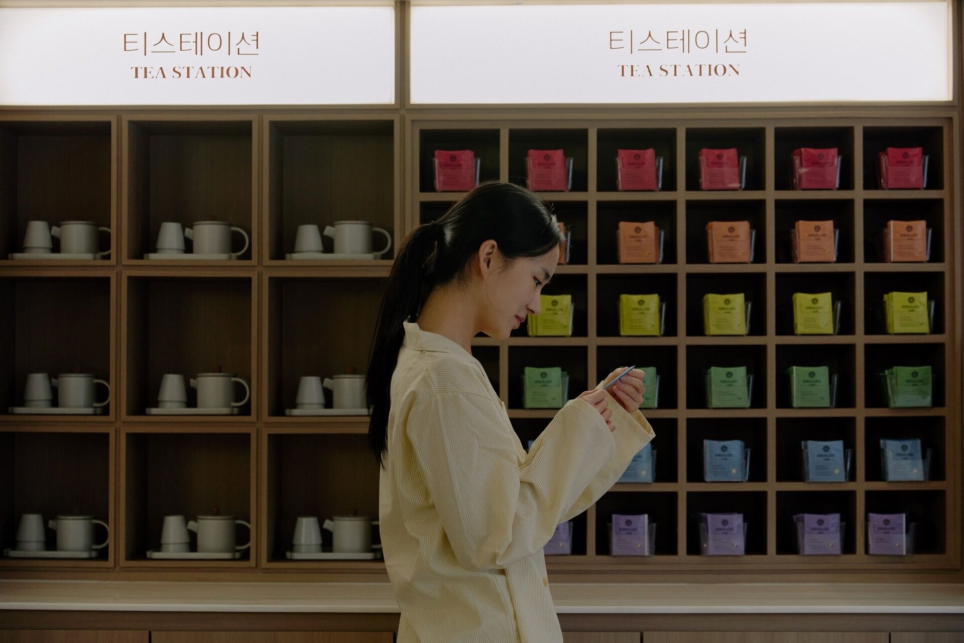 A woman standing in front of a wall with multiple shelves containing various tea products.