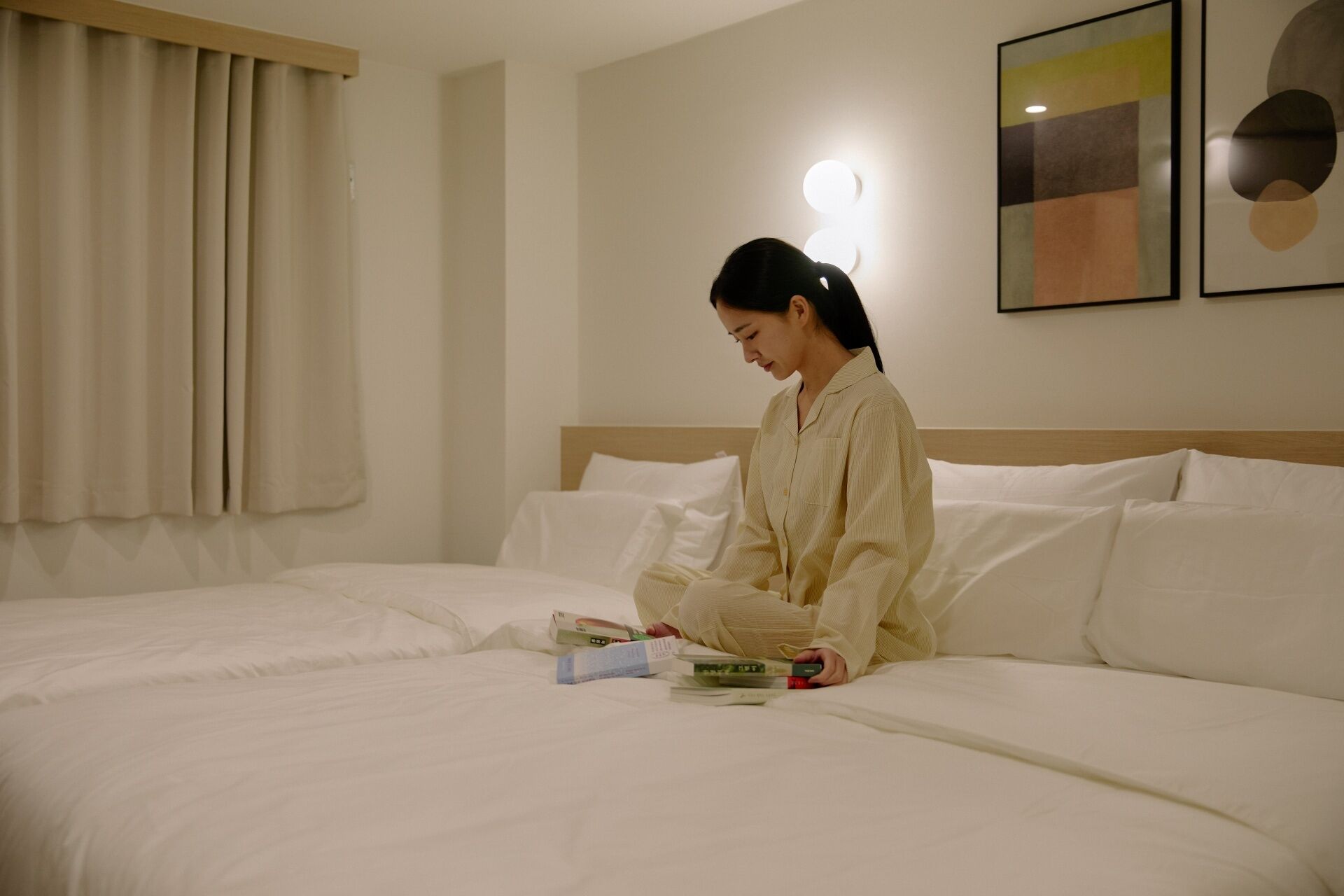 Una persona seduta su un letto in una camera d'hotel, che legge un libro.