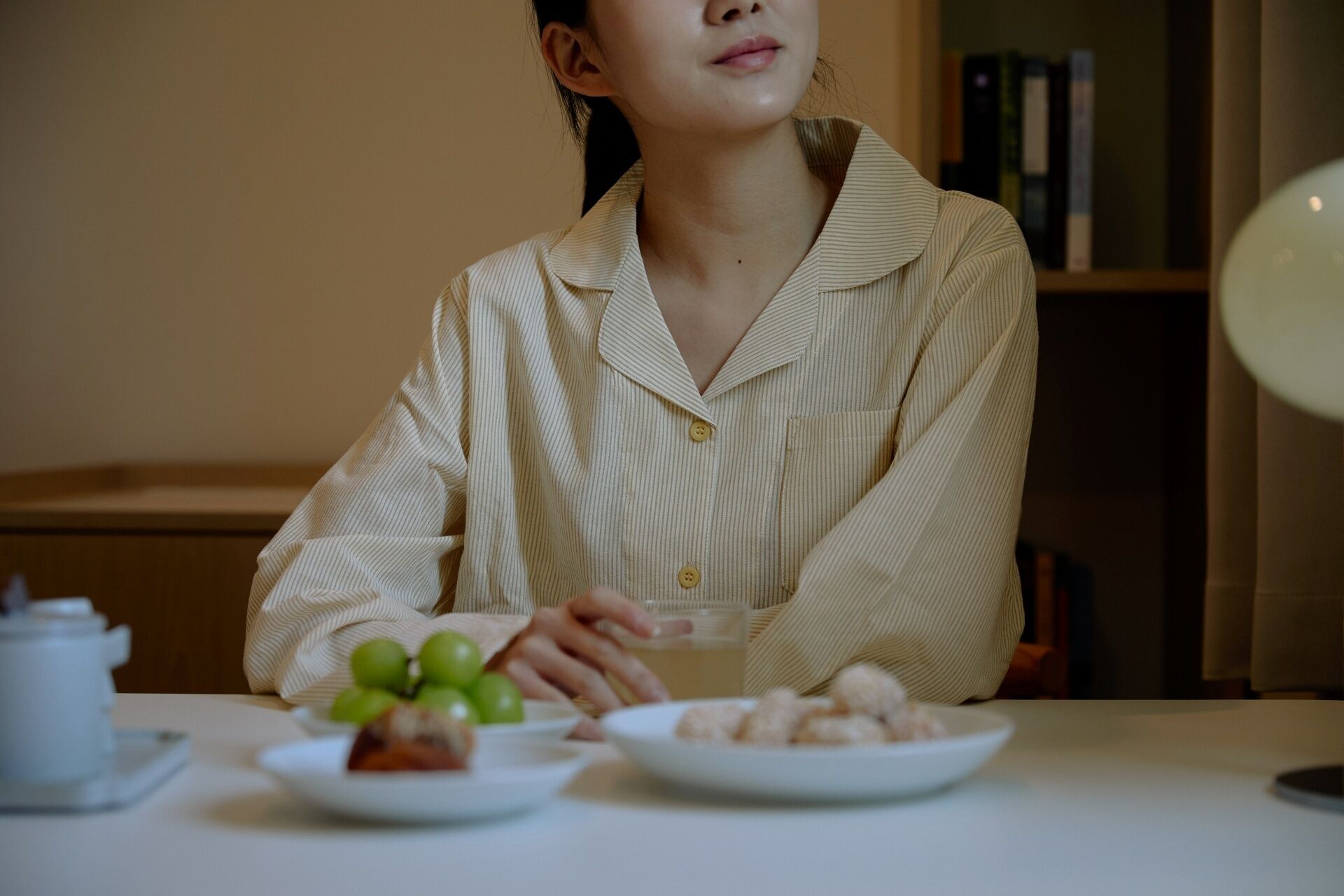 Une personne est assise à une table devant des assiettes de nourriture, une théière et un verre d’eau.