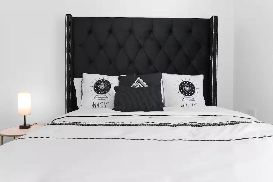 A bed with a black tufted headboard, white bedding, and two decorative pillows with a magic-themed design.