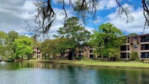 A tranquil outdoor setting with a pond, surrounded by mature trees and multi-story buildings with balconies.