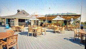 An outdoor patio area with wooden tables and chairs, umbrellas, and a view of the building in the background.