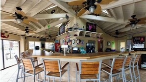 A bar area with a central island, multiple ceiling fans, and bar stools.